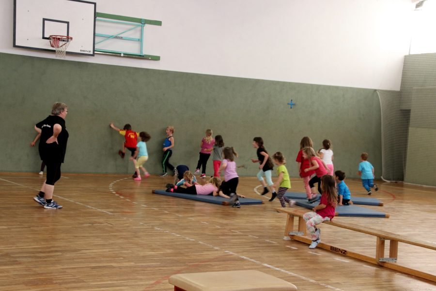 Kinder laufen hinter der Übungsleiterin durch die Turnhalle.