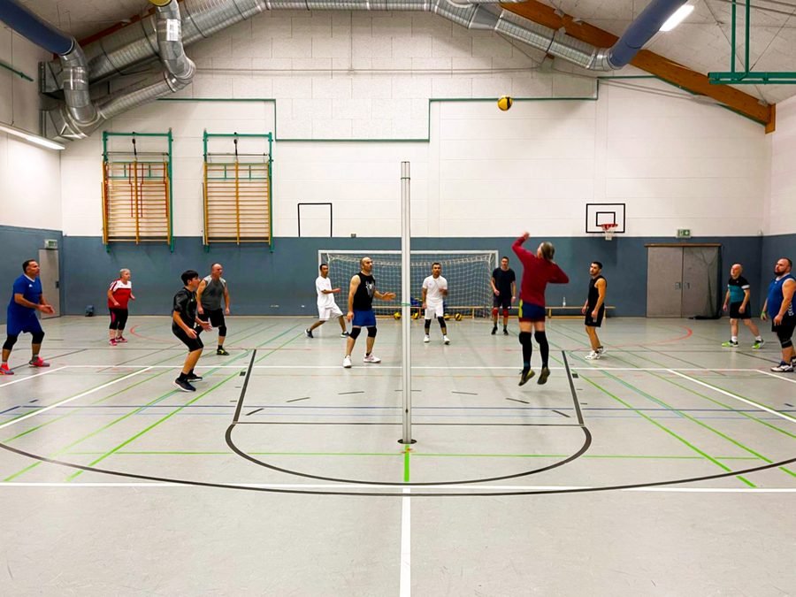 Zwei Mannschaften spielen Volleyball in der Turnhalle.